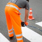 Un ouvrier, en tenue orange de sécurité, est de dos, penché pour enfoncer un câble dans une gaine.